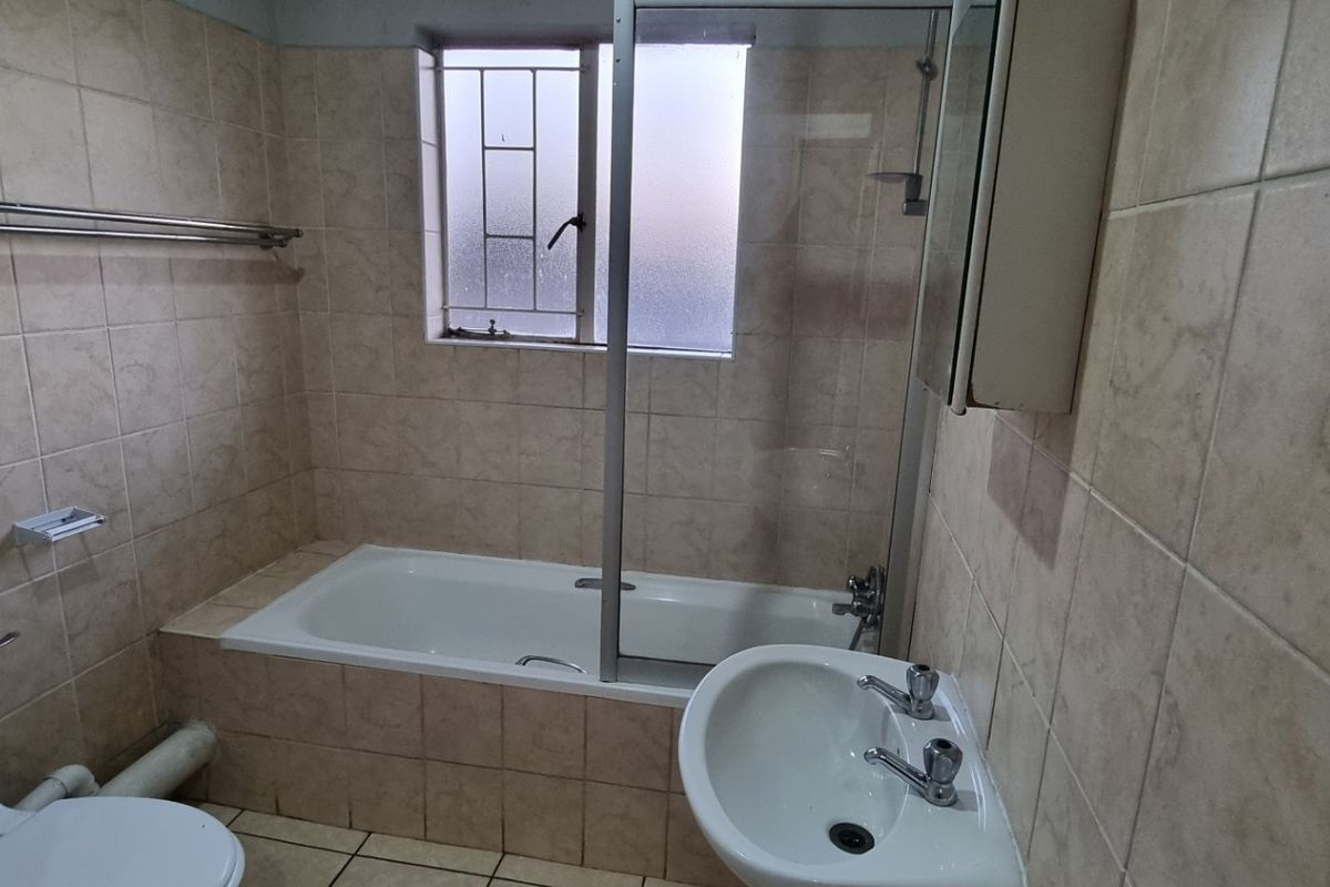 A functional bathroom featuring a bathtub with a shower screen, pedestal basin, and toilet, finished with neutral wall and floor tiling.