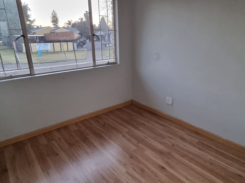 An empty bedroom featuring laminate flooring, neutral walls, and a large steel-framed window providing natural light.
