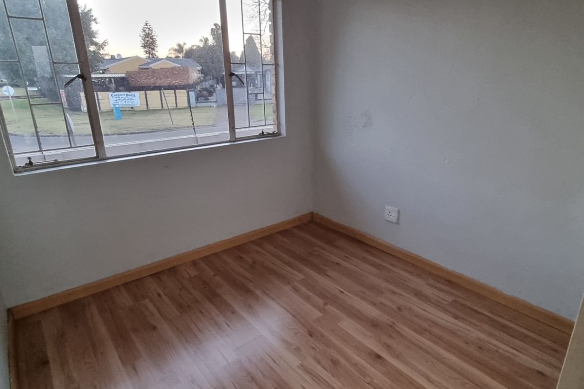 An empty bedroom featuring laminate flooring, neutral walls, and a large steel-framed window providing natural light.
