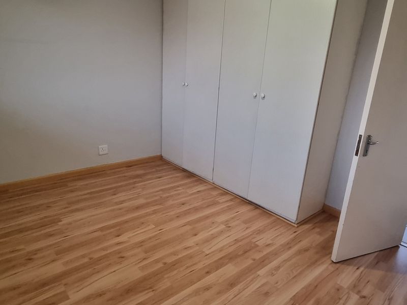 A clean, empty bedroom featuring light-toned laminate flooring and built-in cupboards, with an adjacent view into a tiled bathroom.