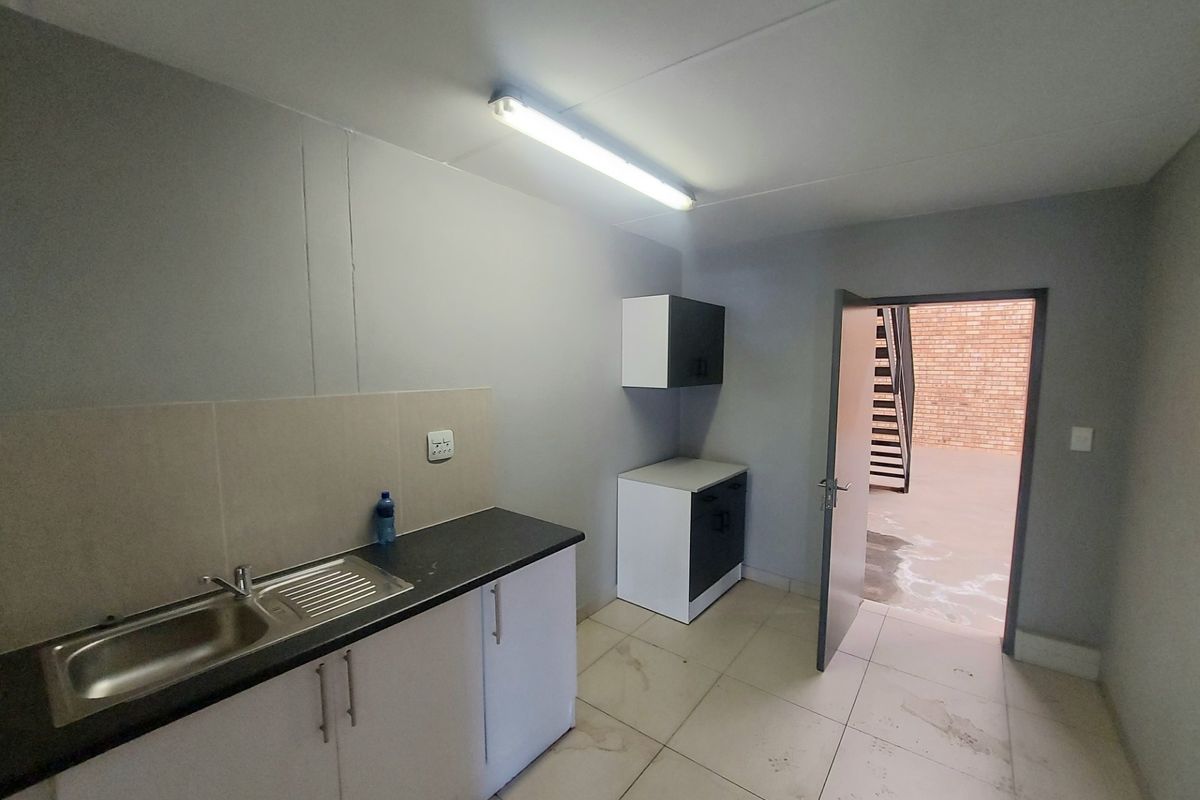 A functional kitchenette area featuring built-in cabinetry, a stainless steel sink, and tiled flooring, with direct access to an outdoor industrial space.