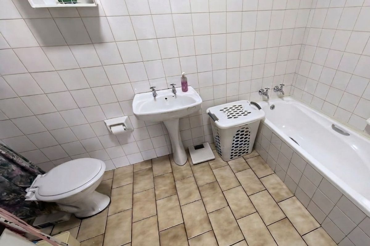 A functional bathroom featuring a pedestal basin, standard toilet, and a bathtub with wall-mounted taps, finished with white wall tiles and tiled flooring.