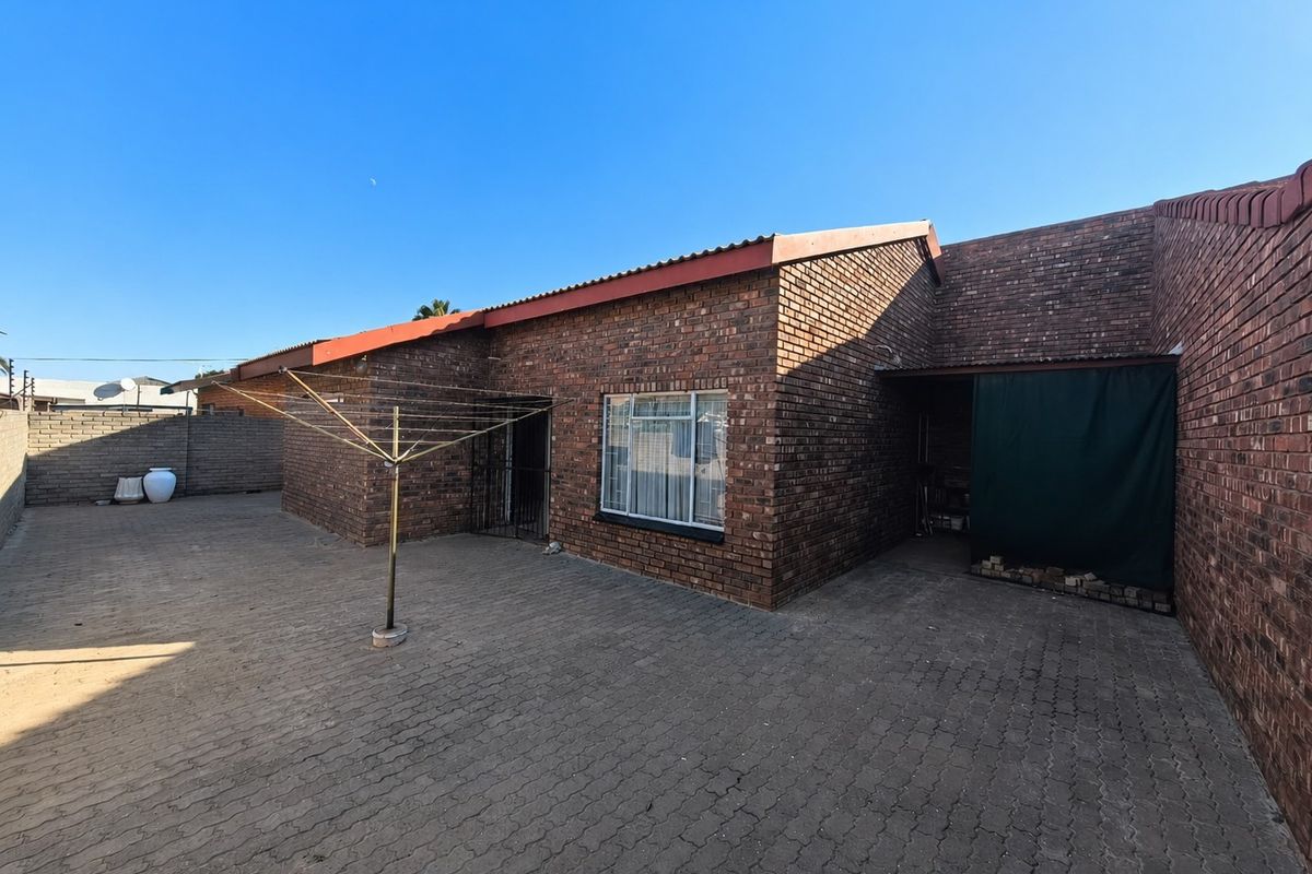 Rear exterior view of a brick townhouse featuring a paved courtyard area and a covered side entrance.