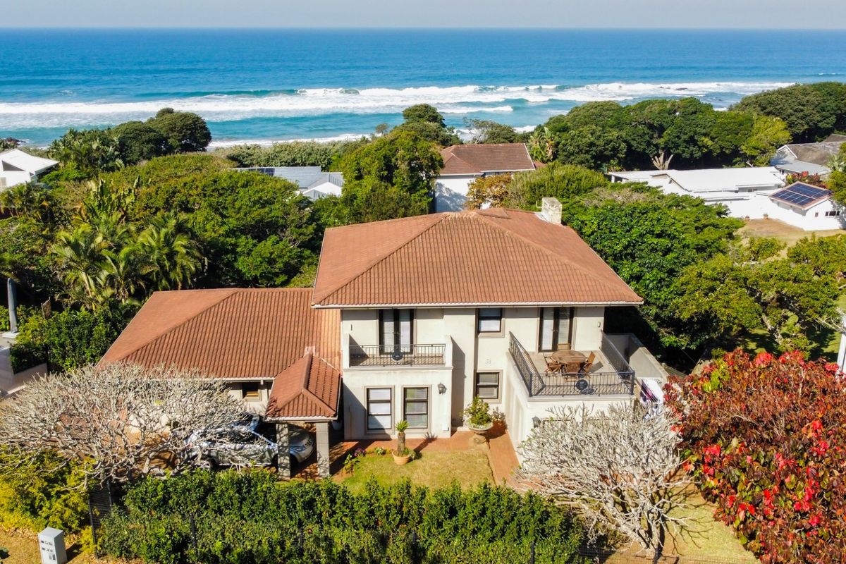 Aerial view of a coastal residence featuring a tiled roof, multiple balconies, and established garden, situated with direct proximity to the ocean.