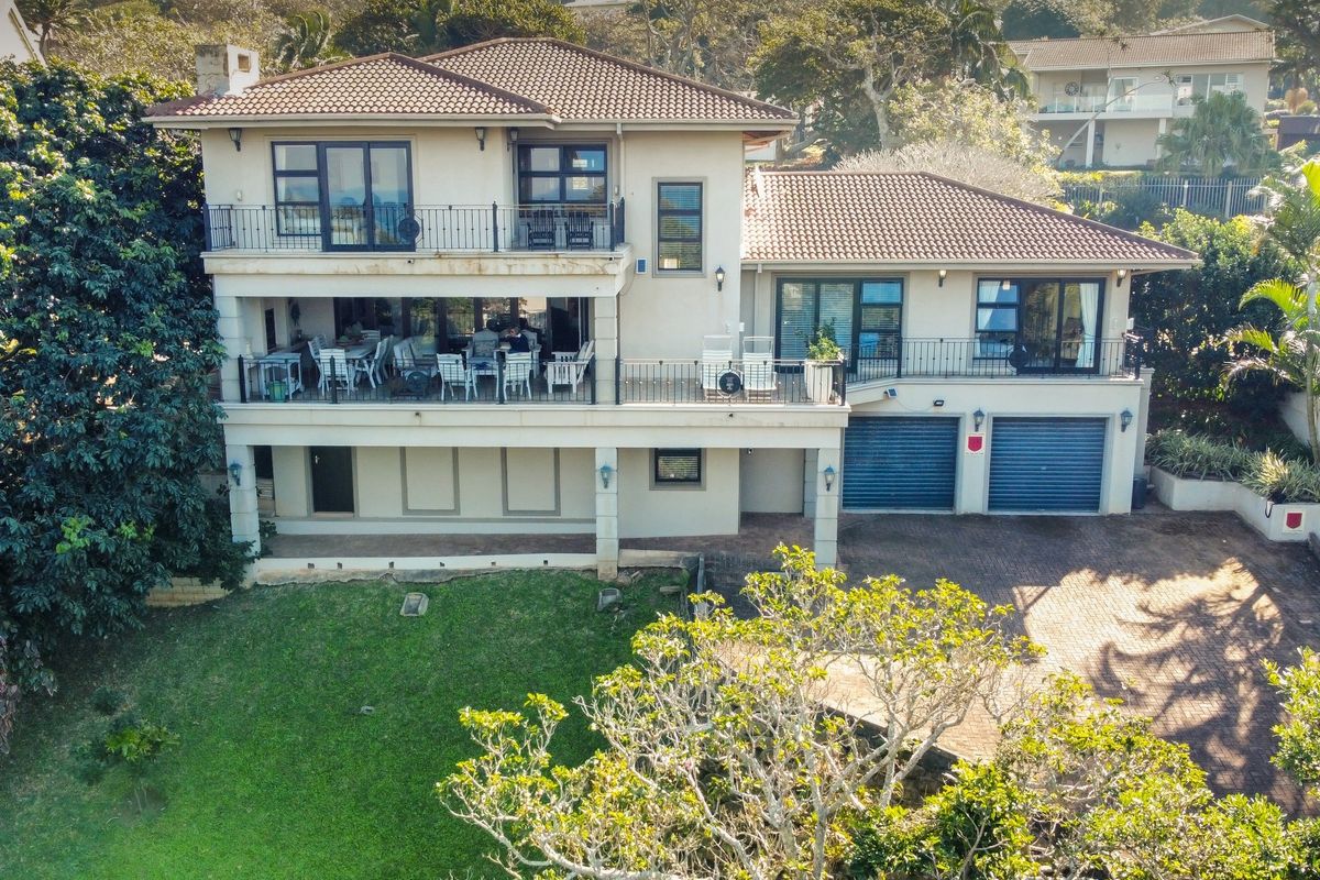 A multi-level residential property featuring a tiled roof, expansive balconies, double garage, and a paved driveway set within a landscaped garden.