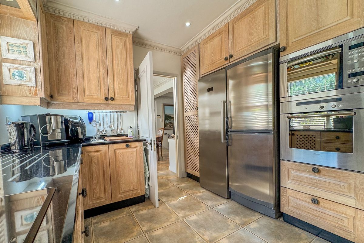 A functional kitchen featuring light wood cabinetry, granite countertops, tiled flooring, and integrated stainless steel appliances including a double oven and refrigerator.
