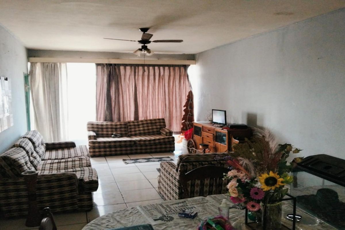 A spacious living room featuring tiled flooring, a ceiling fan, and large windows with curtains, offering a functional layout for relaxation.