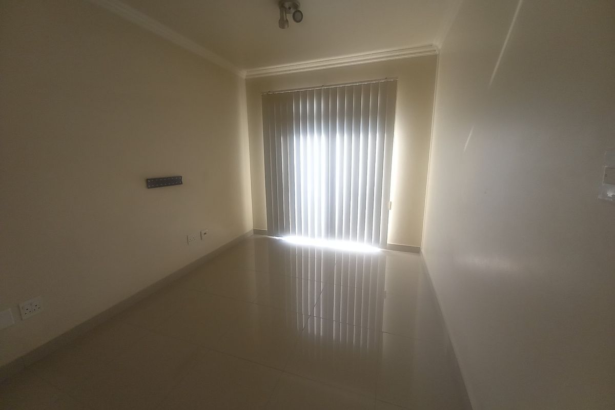 An empty living room featuring tiled flooring, neutral walls, and vertical blinds covering the sliding door access.