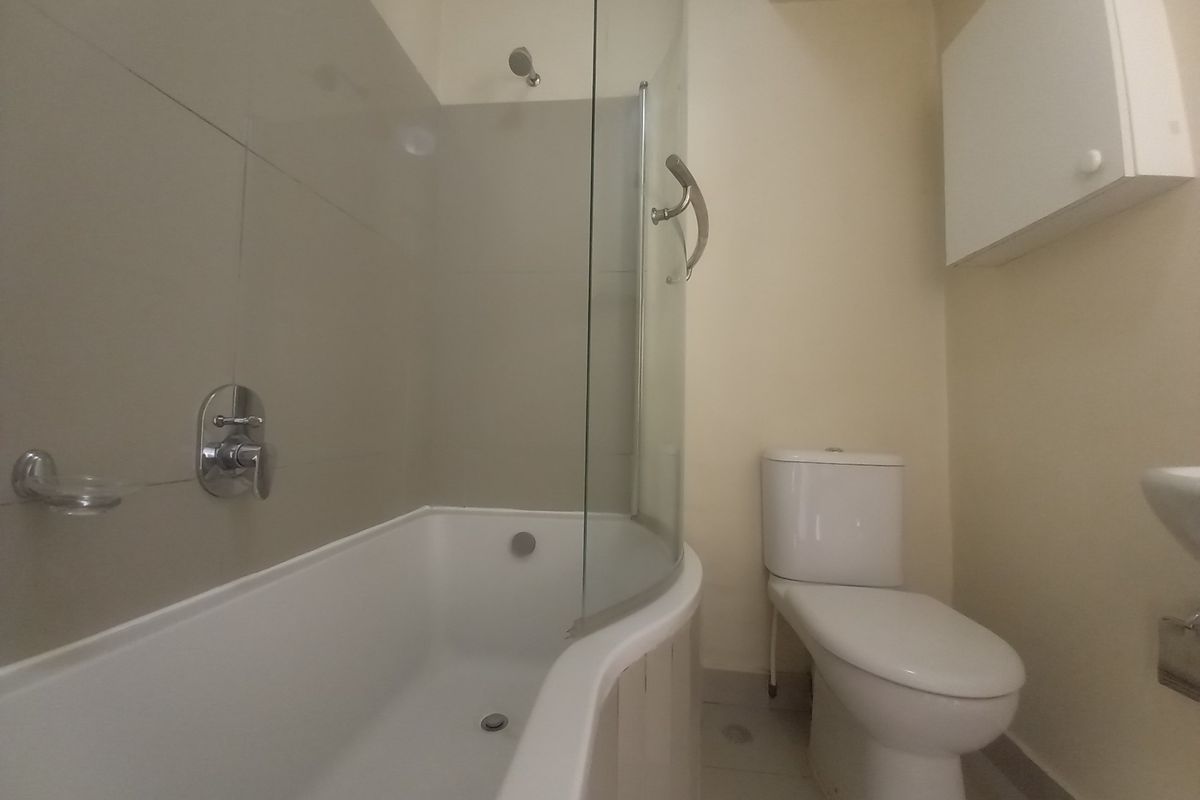 A functional bathroom featuring a shower-over-bath combination with a glass screen, a standard toilet, and a wall-mounted storage cabinet.