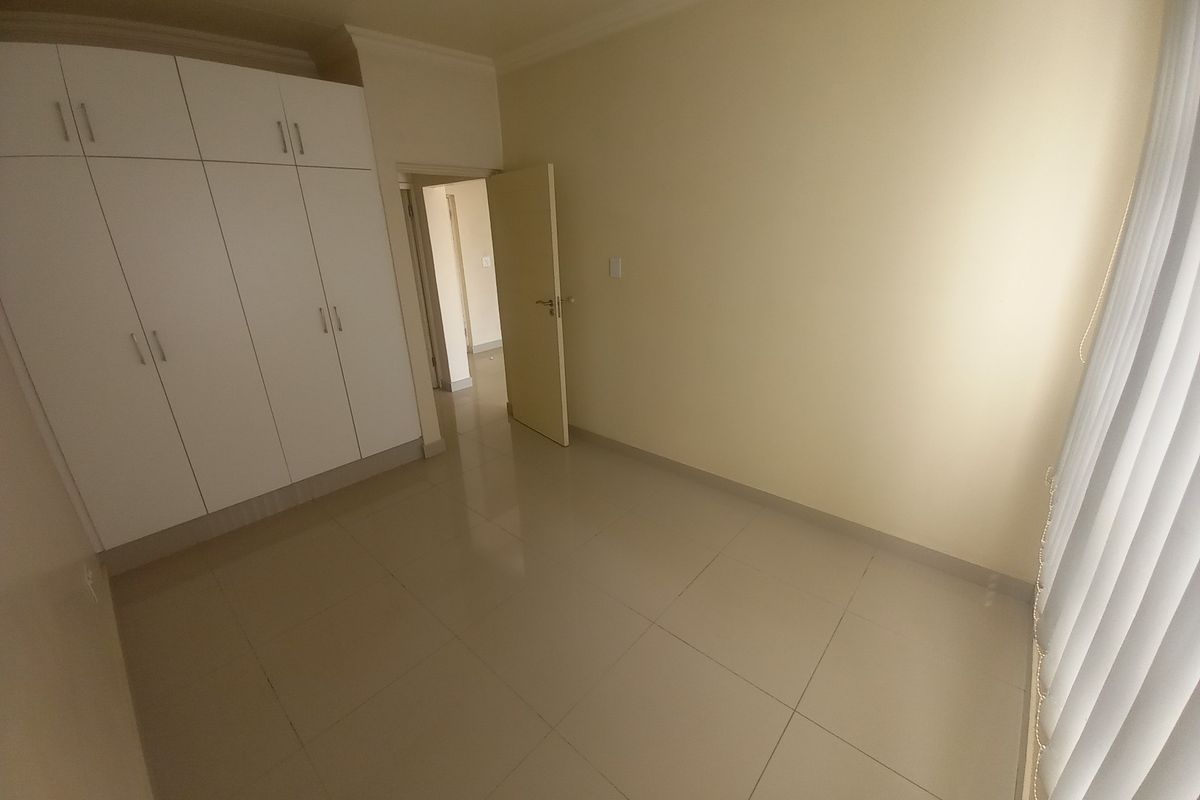 A bright, empty bedroom featuring neutral tiled flooring and built-in white cabinetry, offering a clean and versatile space.