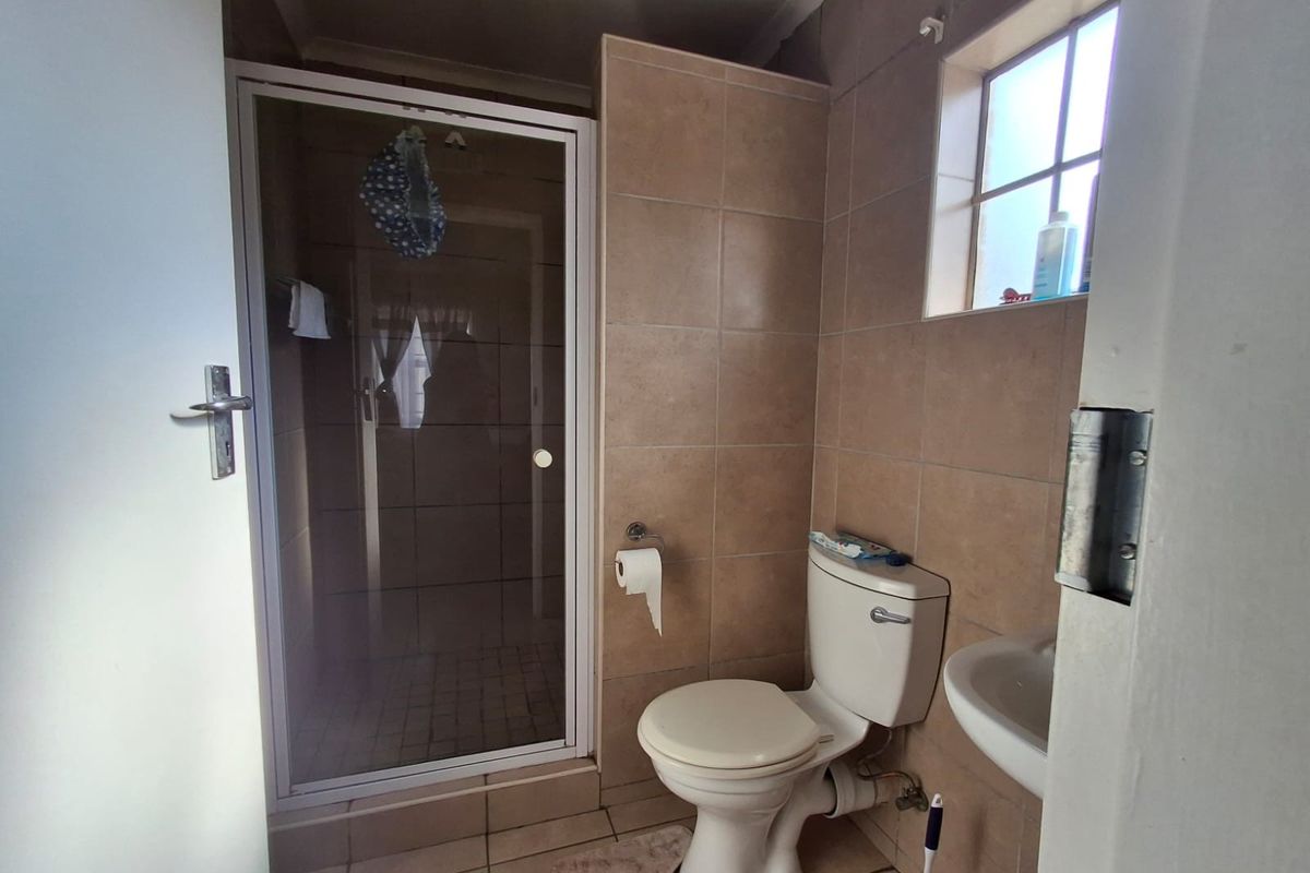 Compact bathroom featuring a shower enclosure, toilet, and washbasin with neutral wall and floor tiling.