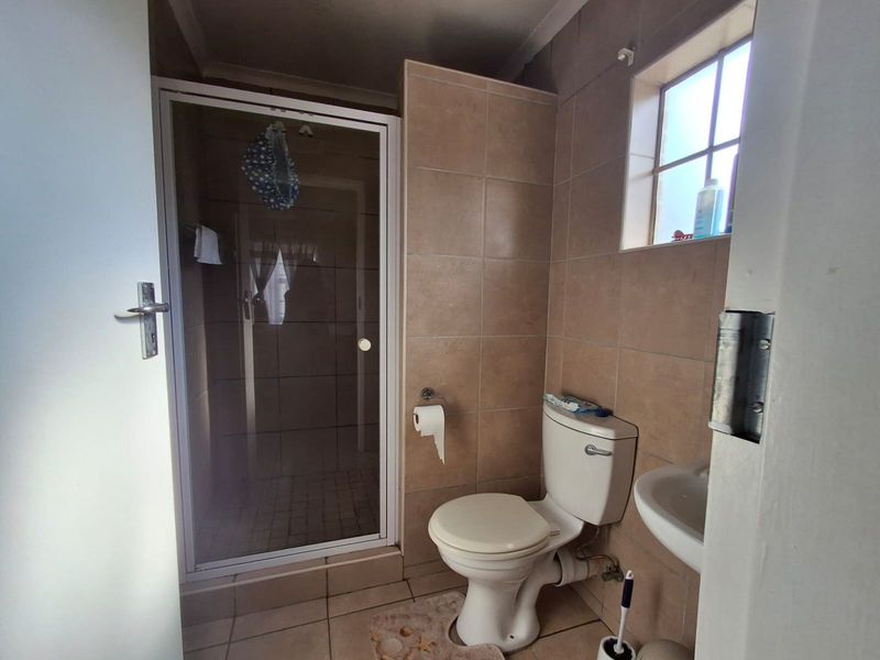 Compact bathroom featuring a shower enclosure, toilet, and washbasin with neutral wall and floor tiling.