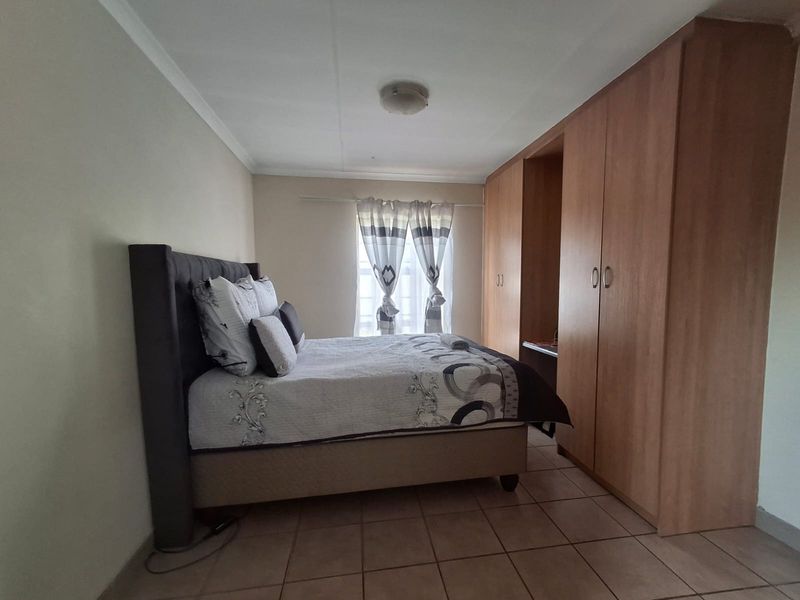 A functional bedroom featuring built-in wooden cupboards, tiled flooring, and a coved ceiling, providing a practical and well-maintained living space.