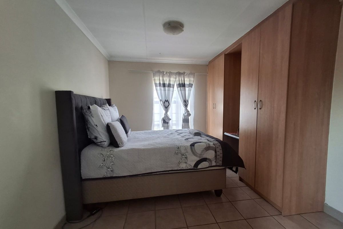 A functional bedroom featuring built-in wooden cupboards, tiled flooring, and a coved ceiling, providing a practical and well-maintained living space.