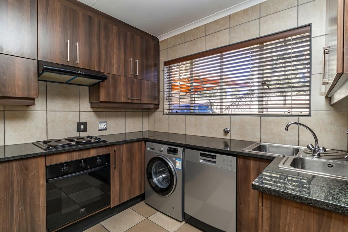 A functional kitchen featuring dark wood cabinetry, granite countertops, a built-in oven, hob, extractor fan, and integrated space for laundry and dishwashing appliances.