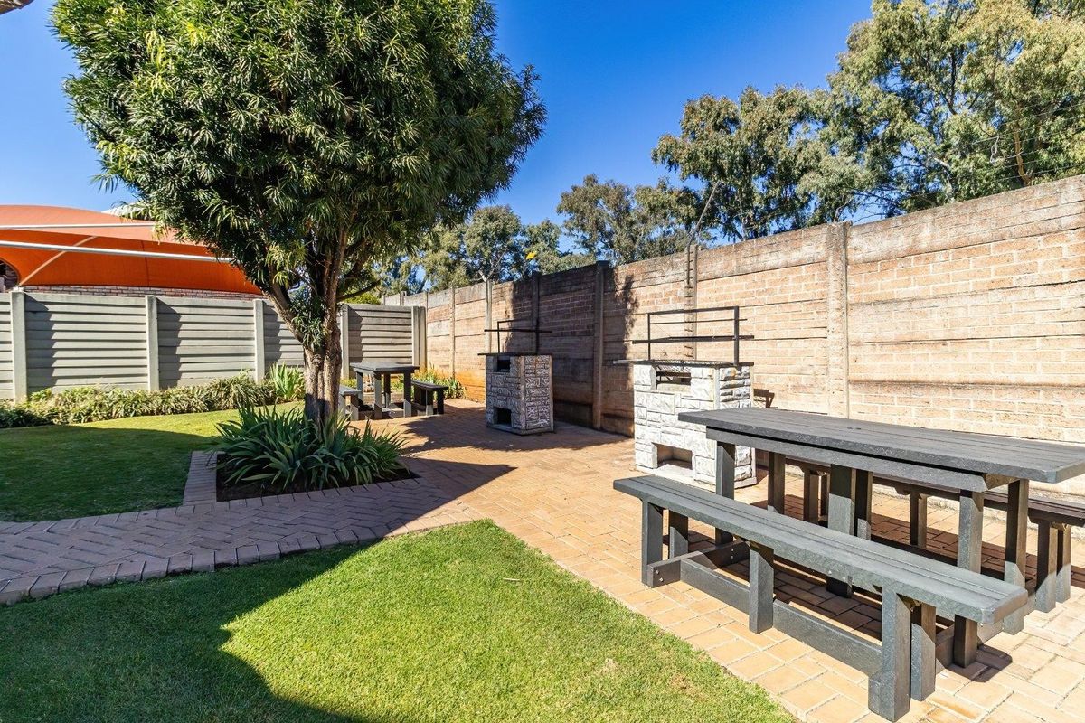 A well-maintained rear garden featuring a paved patio area with built-in brick braai facilities, surrounded by perimeter walling and established landscaping.