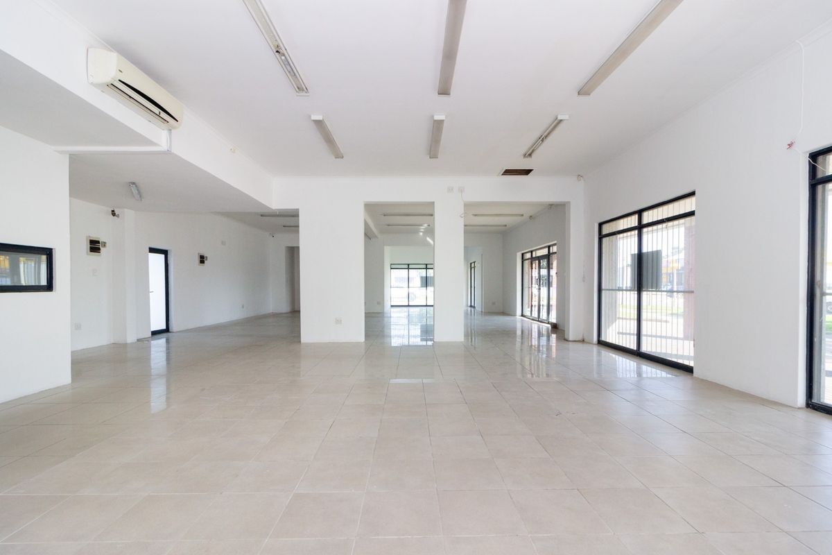 Spacious open-plan commercial area featuring neutral tiled flooring, ample natural light through large windows, and wall-mounted air conditioning.