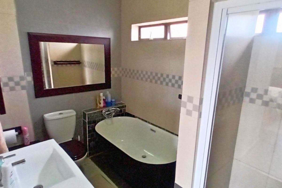 A functional bathroom featuring a built-in bathtub, a separate shower enclosure, a wall-mounted vanity basin, and a toilet with tiled wall accents.