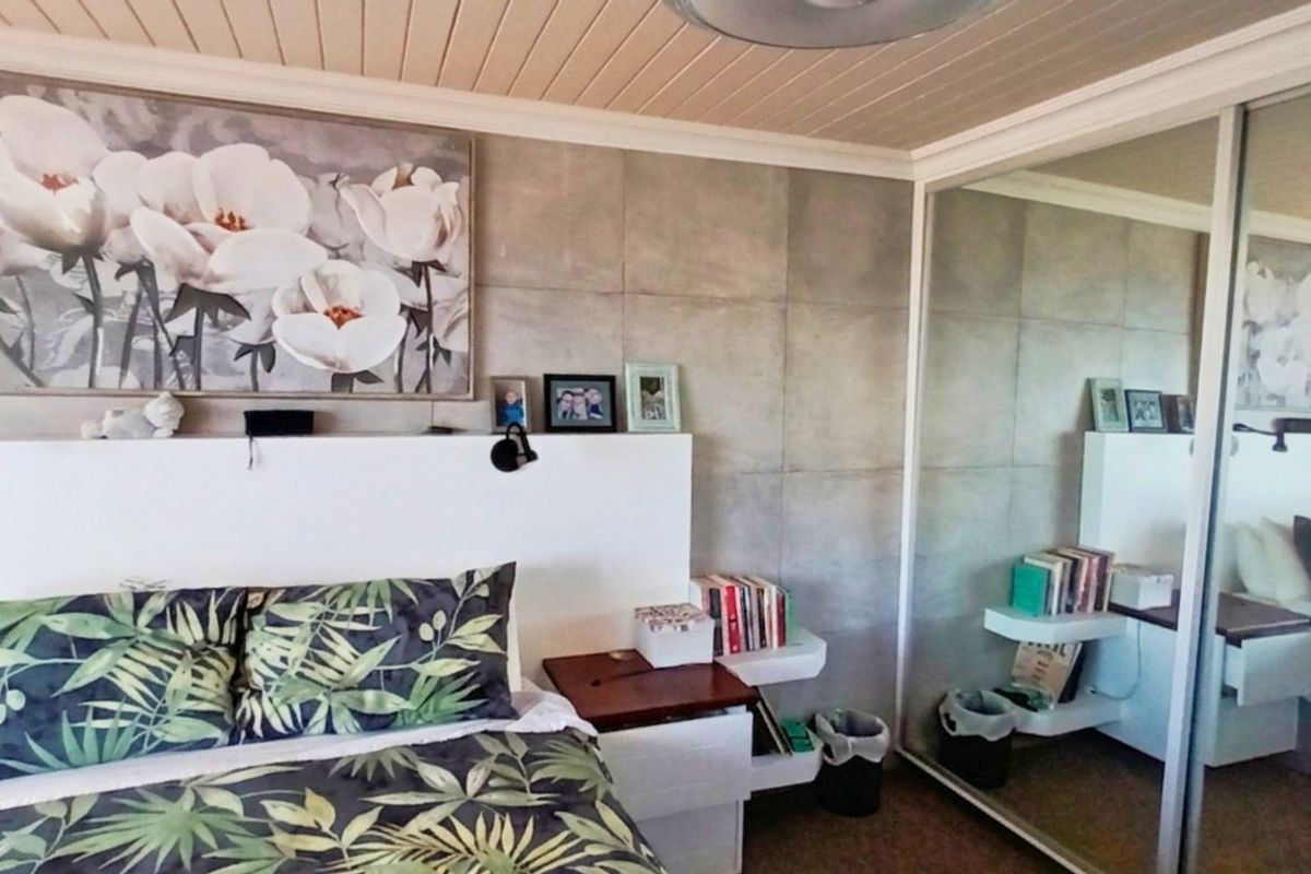 A bedroom featuring a built-in wardrobe with mirrored sliding doors, a tiled feature wall, and a tongue-and-groove timber ceiling.