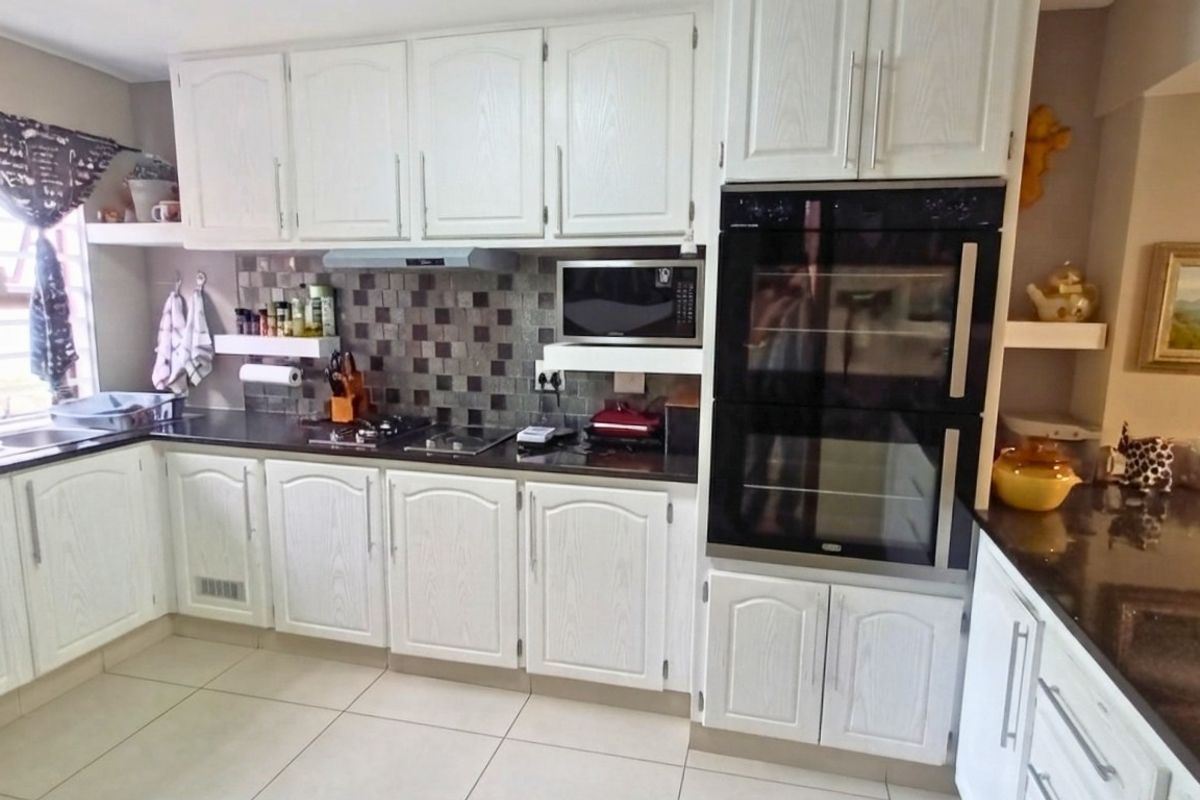 A functional kitchen featuring white cabinetry, dark granite countertops, a mosaic tile backsplash, and a built-in double oven.