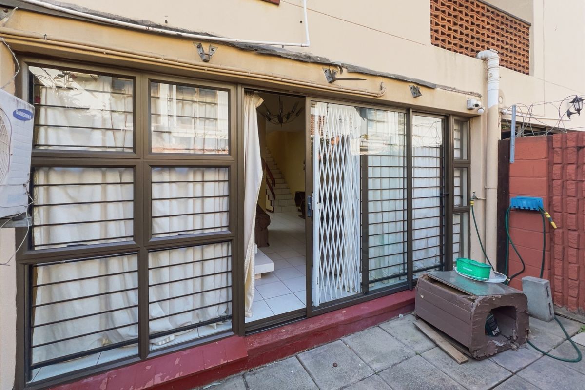 Rear exterior view of the townhouse featuring sliding glass doors with security gates, tiled patio area, and external wall-mounted air conditioning unit.