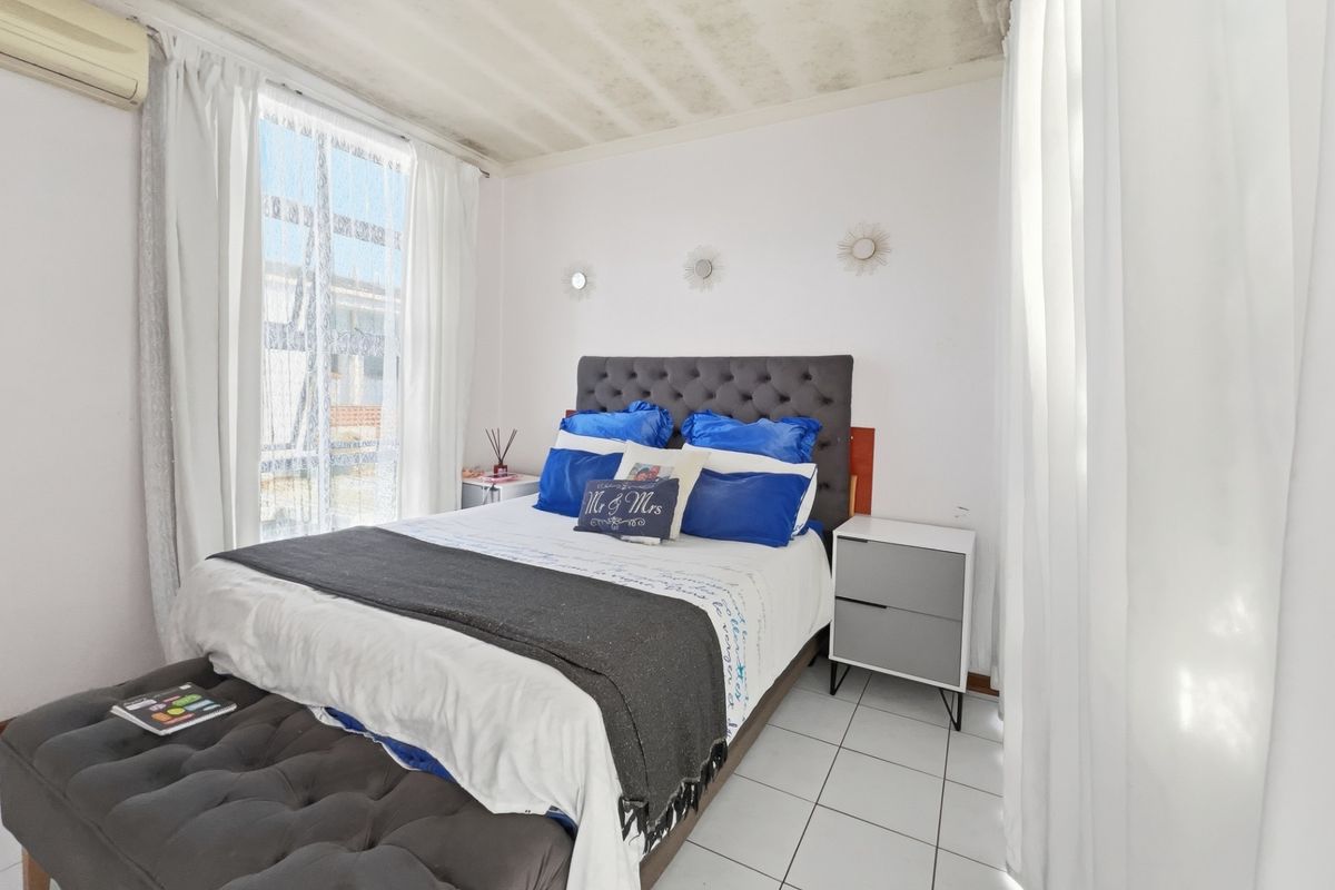 A bedroom featuring tiled flooring, a wall-mounted air conditioning unit, and large windows allowing natural light.