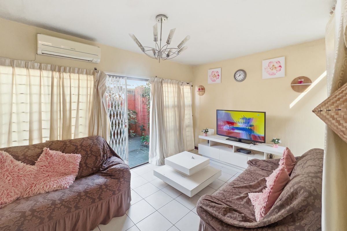 A comfortable living room featuring tiled flooring, a wall-mounted air conditioning unit, and sliding glass doors that open to a private outdoor patio area.