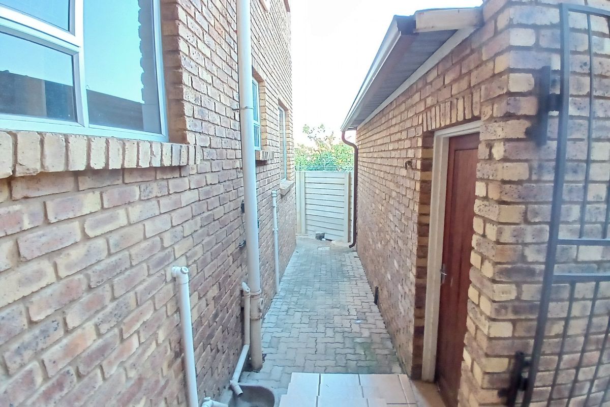 A narrow side passage featuring face-brick walls, paved flooring, and external drainage pipes, providing access between the main structure and an outbuilding.