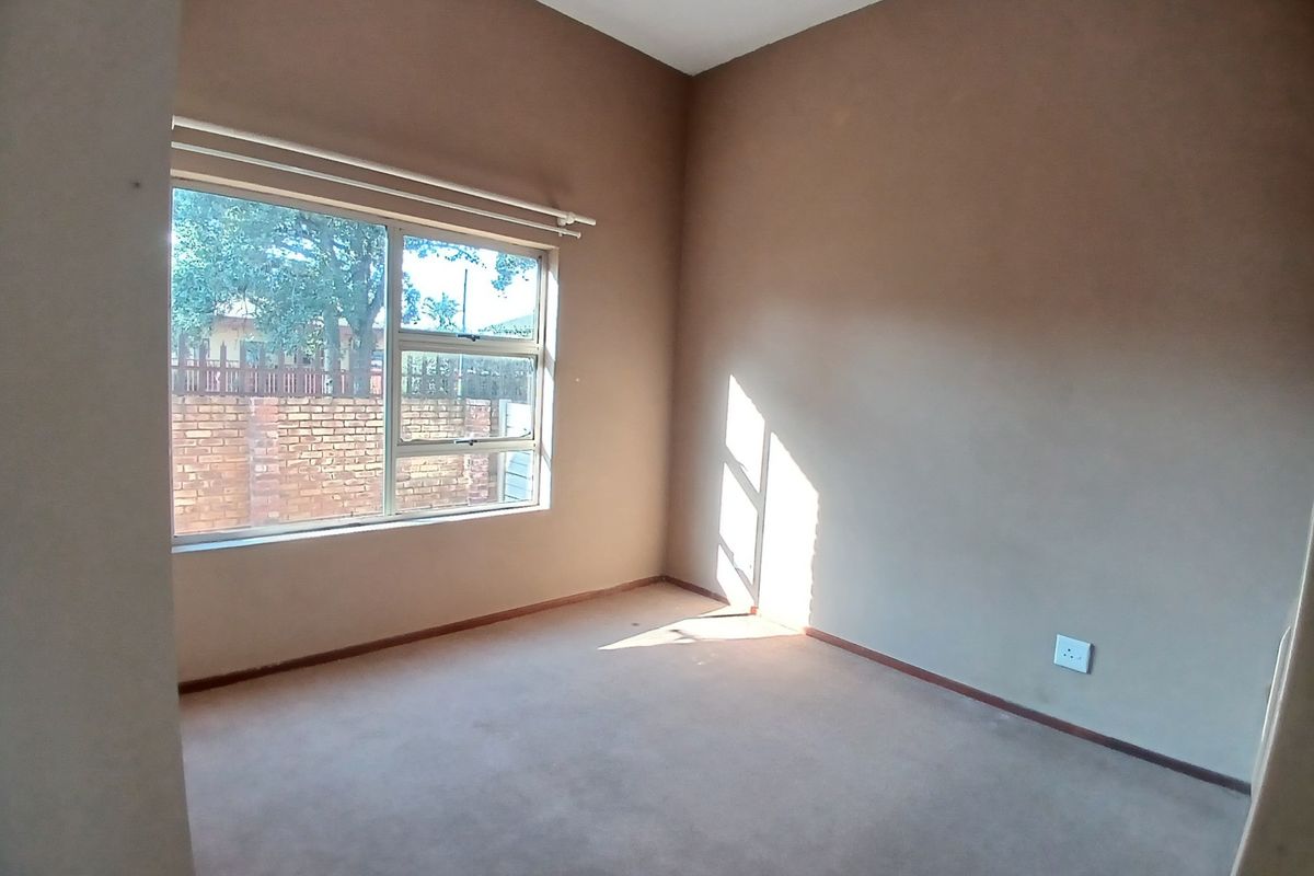 An empty bedroom featuring neutral wall tones, carpeted flooring, and a large window providing natural light.