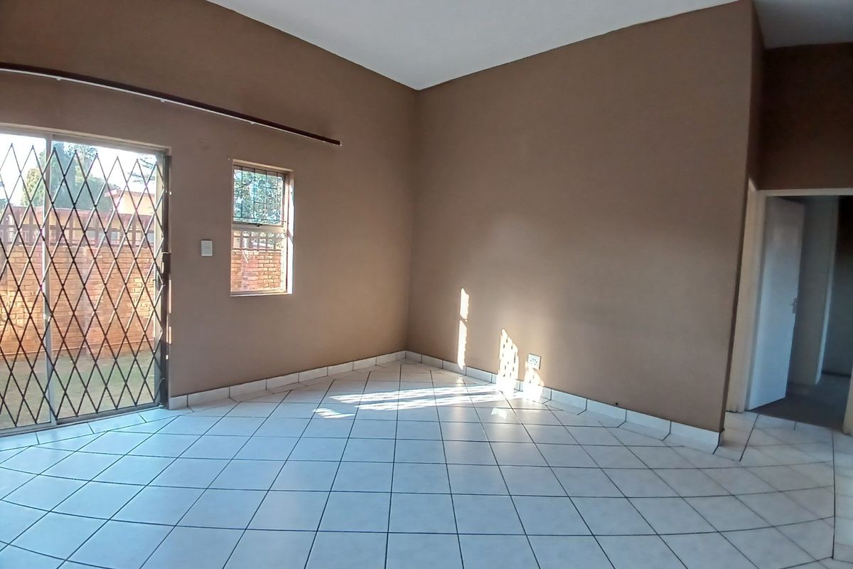 An empty living room featuring tiled flooring, a sliding glass door with security gate, and natural light through a side window.