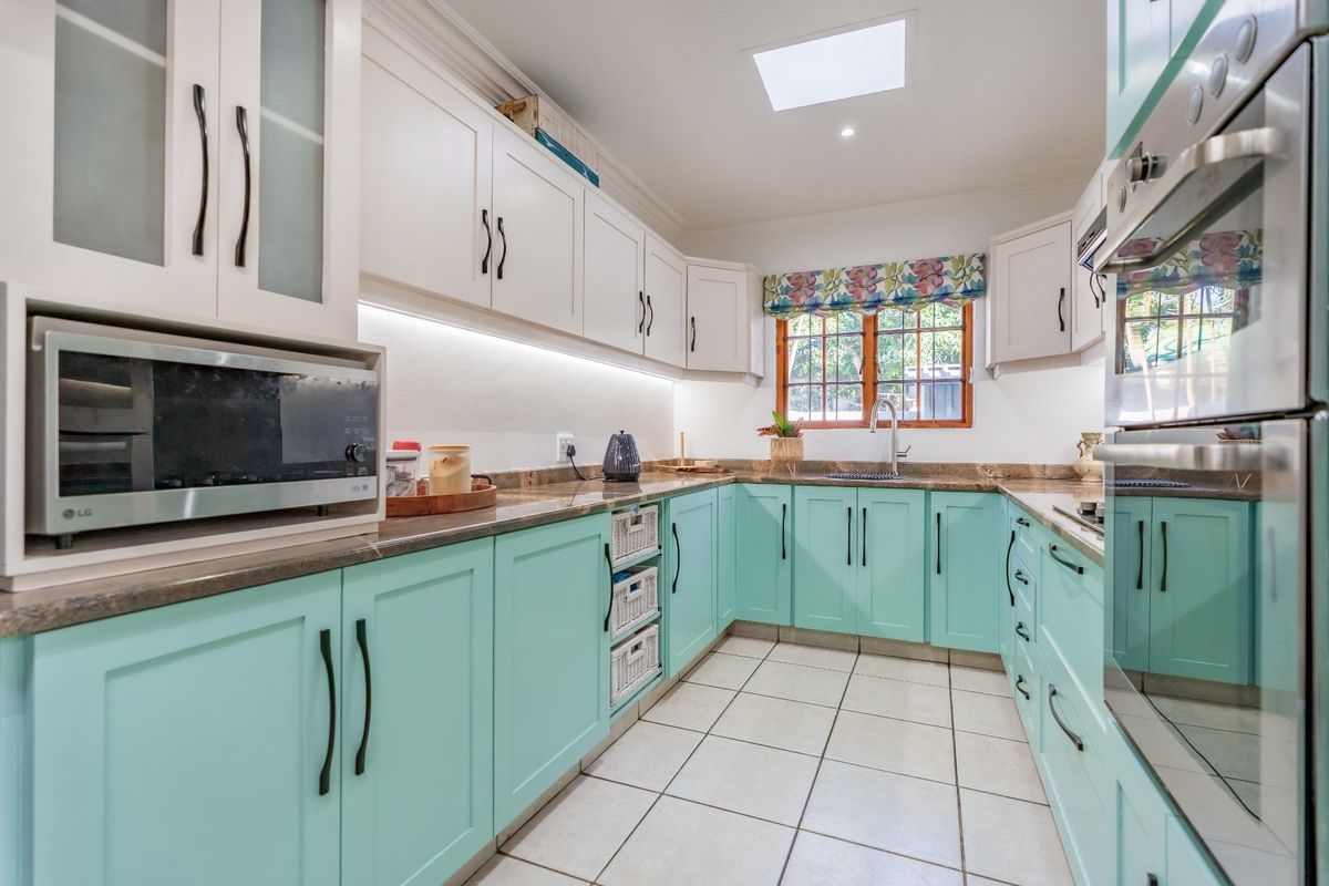 A well-lit kitchen featuring two-tone cabinetry, stone countertops, integrated oven, and a skylight, providing a functional and bright workspace.
