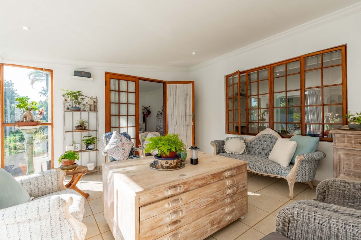A bright and airy living room featuring tiled flooring, recessed lighting, and classic timber-framed glass doors that provide access to the outdoor area.