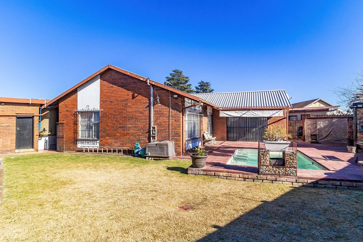 Rear exterior view featuring a brick house, a paved patio area, a swimming pool, and a lawn.