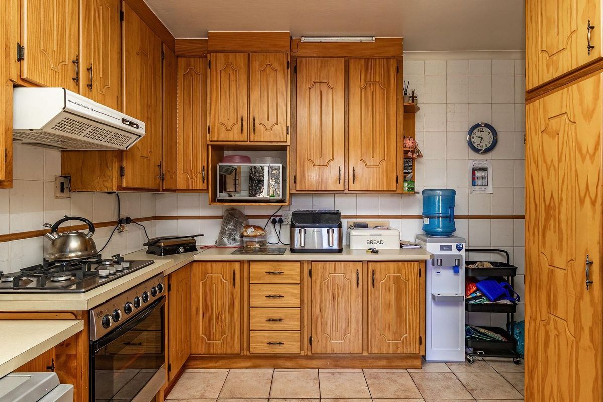 A functional kitchen featuring traditional wooden cabinetry, a built-in gas hob, oven, and extractor fan with tiled splashbacks and flooring.