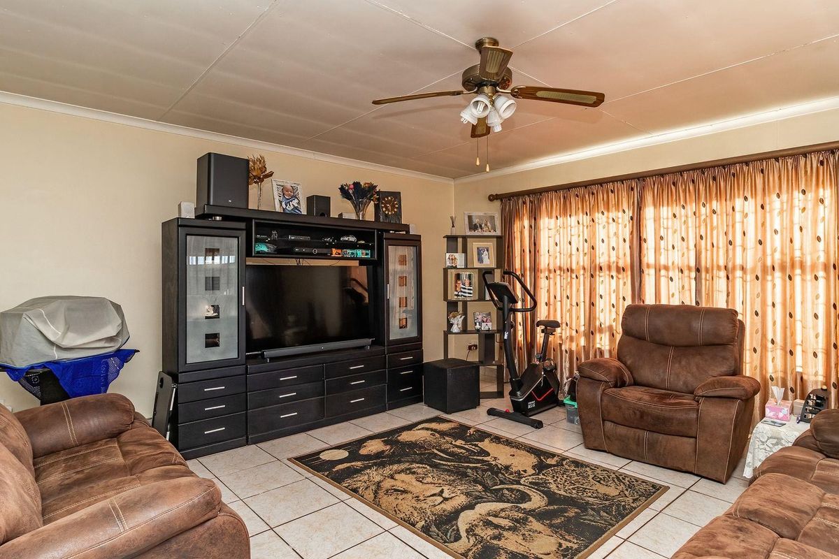 A living room featuring tiled flooring, a ceiling fan, and large windows with curtains, providing a functional and comfortable living space.
