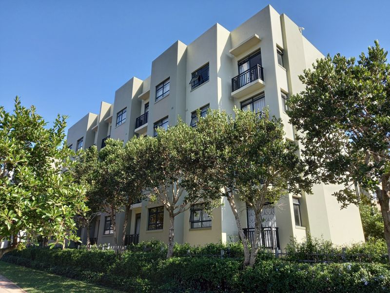 A modern multi-story apartment building featuring a clean concrete facade, private balconies, and well-maintained surrounding landscaping.