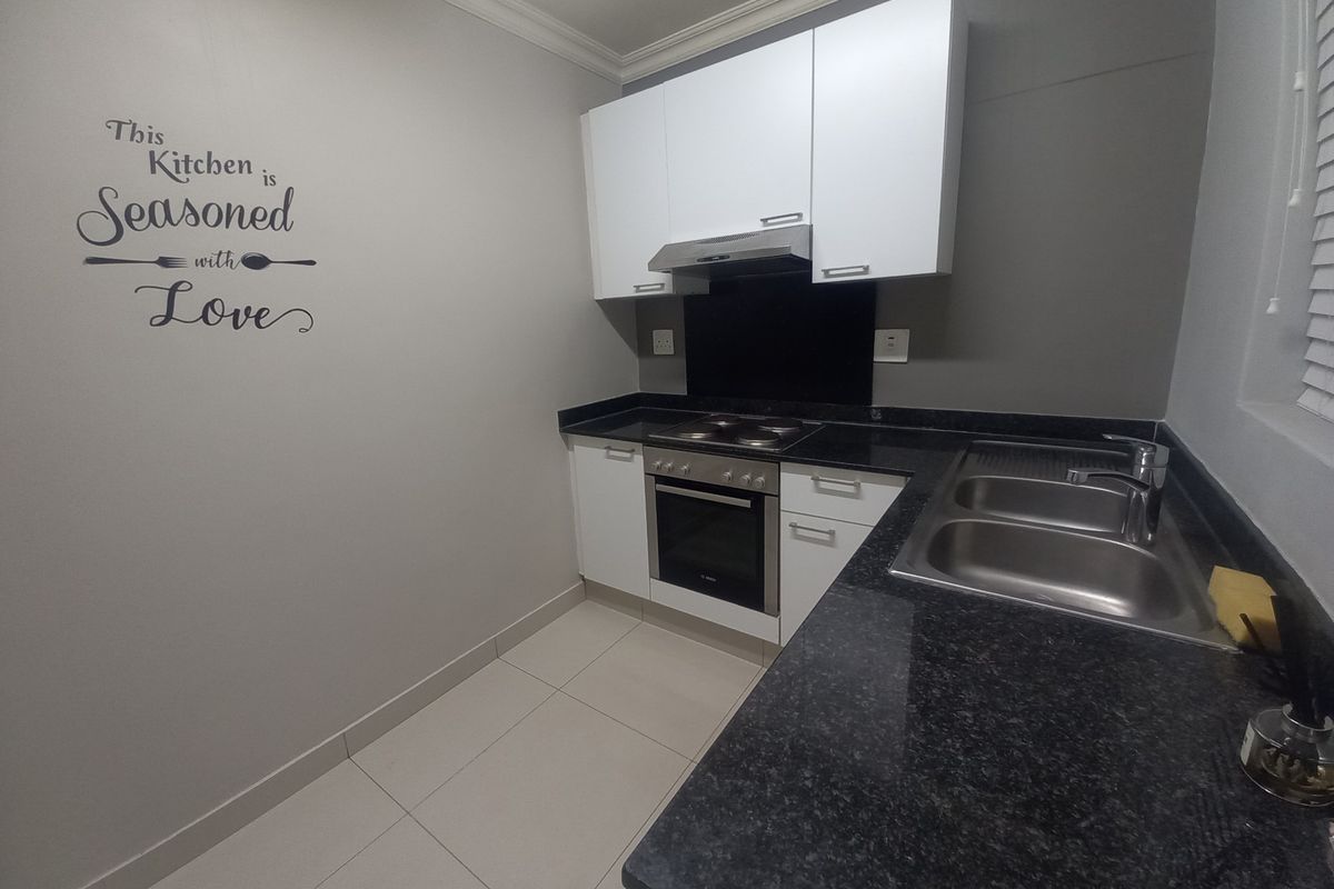 A compact kitchen featuring white cabinetry, dark granite countertops, a built-in oven, electric hob, extractor fan, and a double stainless steel sink.