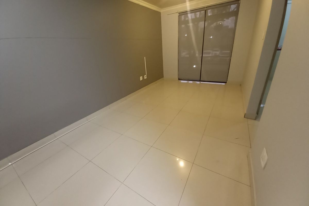 An empty living room featuring large format floor tiles, a grey accent wall, and sliding glass doors with roller blinds.