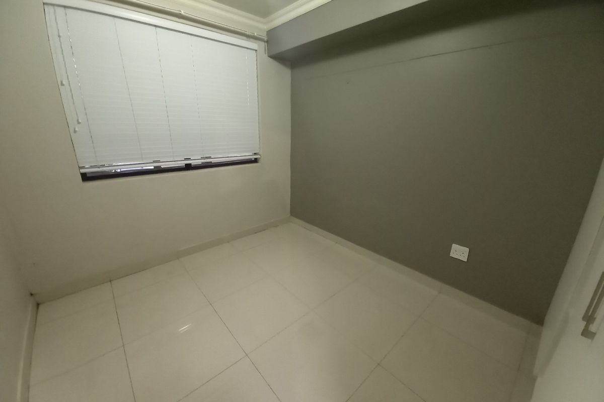 A clean, empty bedroom featuring neutral tiled flooring, a grey accent wall, and fitted window blinds.