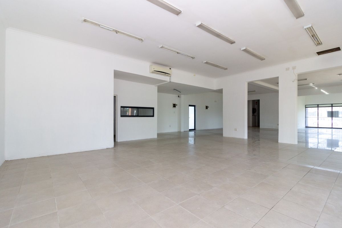 Spacious open-plan retail area featuring neutral tiled flooring, recessed fluorescent lighting, and a wall-mounted air conditioning unit.