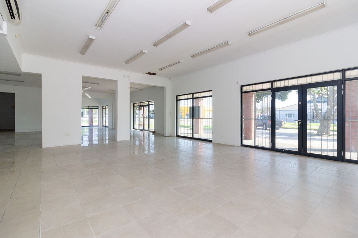 Spacious open-plan retail area featuring tiled flooring, large glass storefront windows with security gates, and integrated air conditioning.