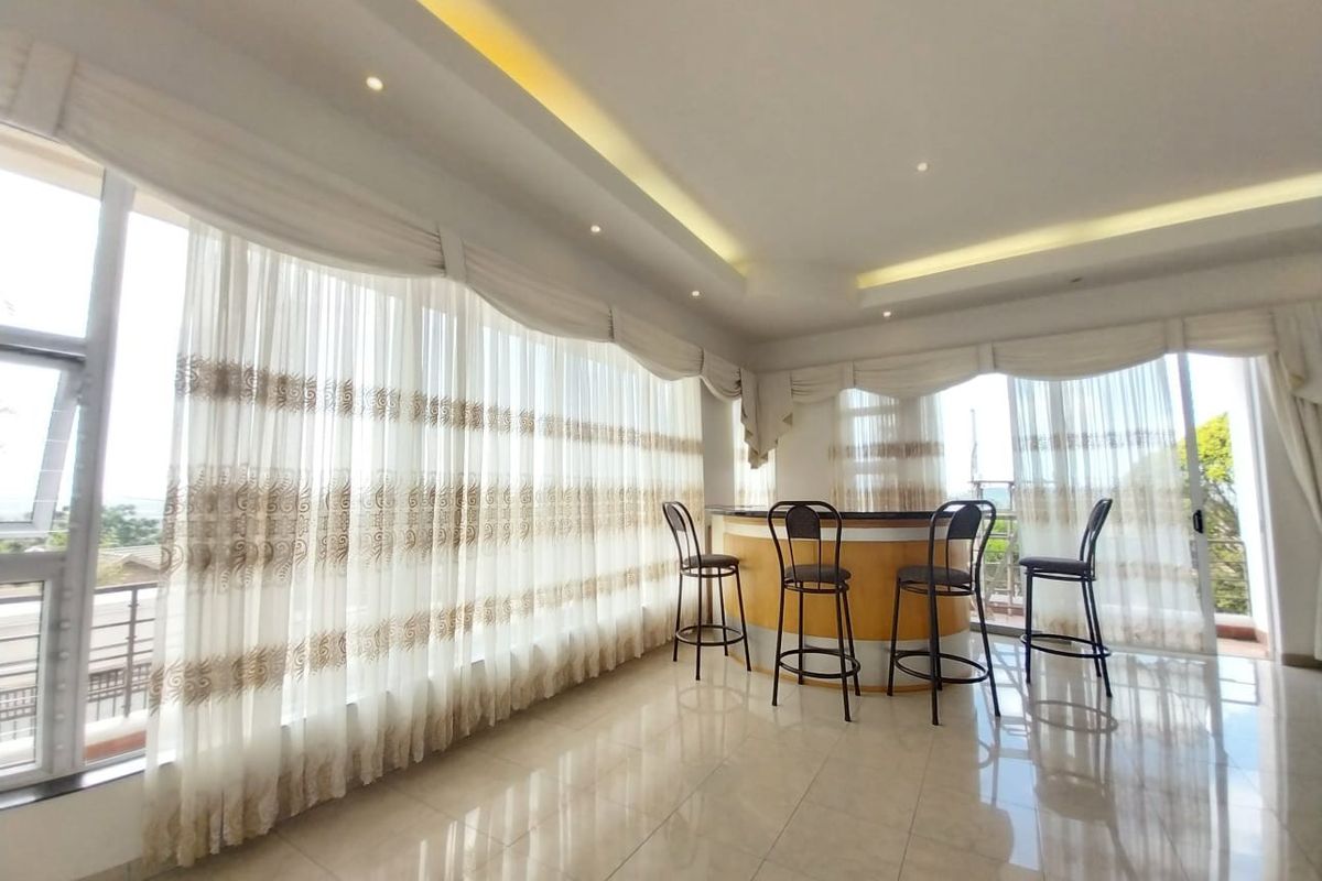 Spacious living area featuring a built-in circular bar, recessed ceiling lighting, and expansive floor-to-ceiling windows with elegant drapery.