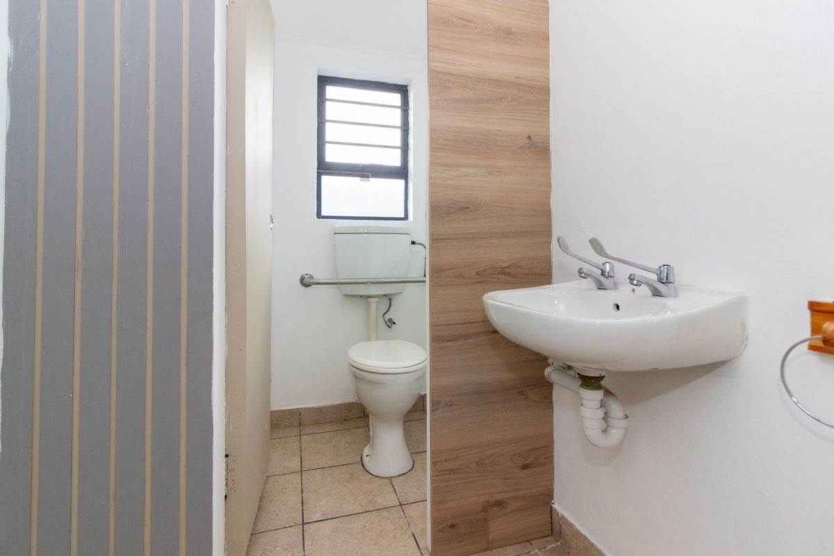 A functional bathroom featuring a wall-mounted basin, toilet with grab rail, and tiled flooring.