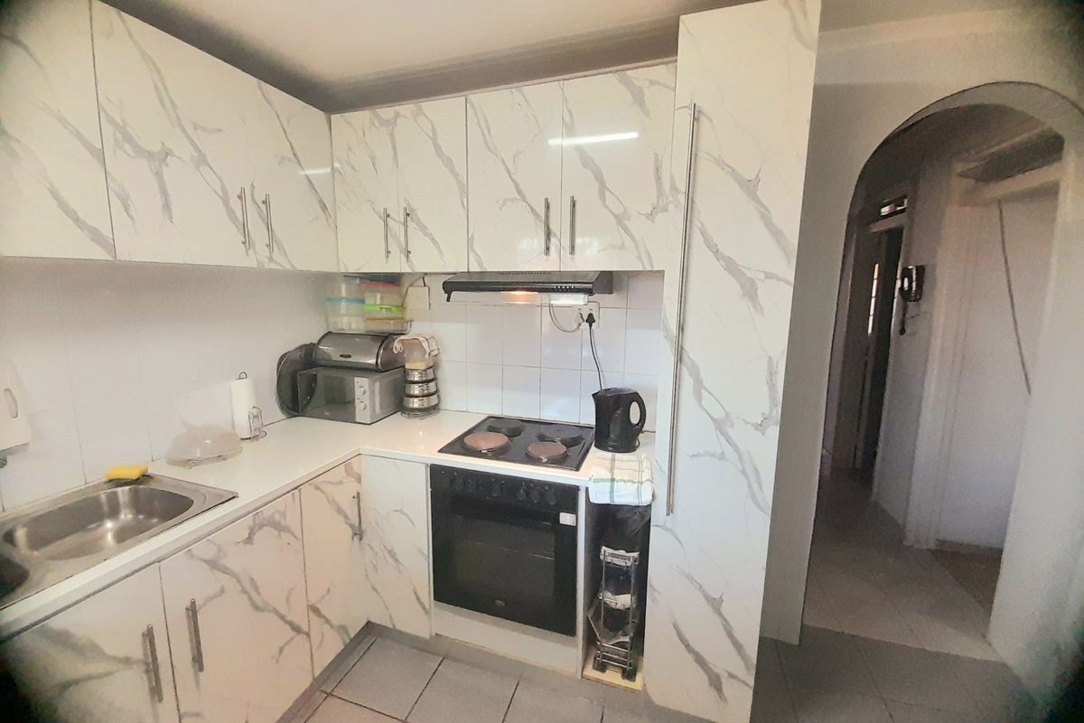 Compact kitchen featuring marble-effect cabinetry, built-in oven with electric hob, extractor fan, and tiled flooring.