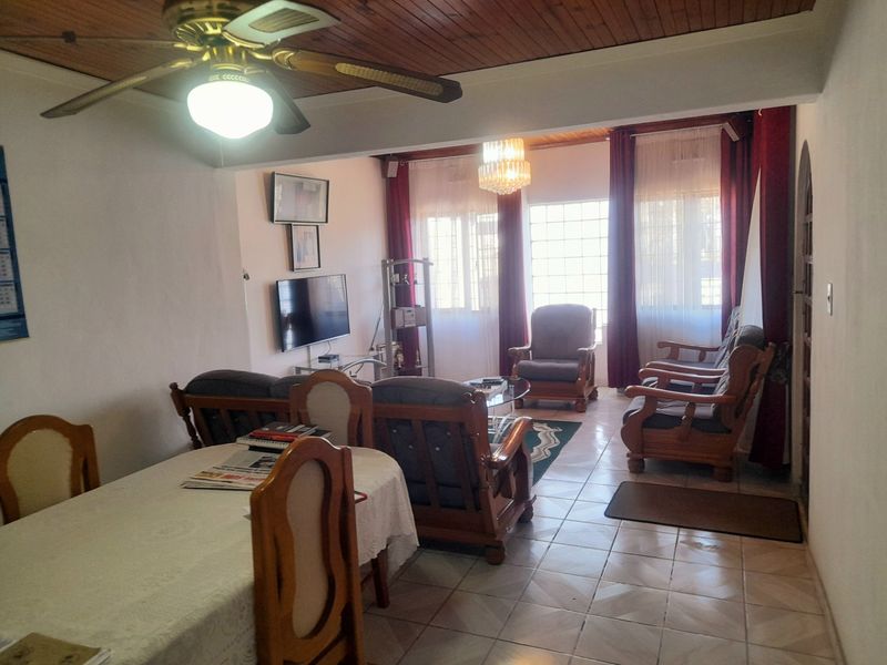 Open plan living and dining area featuring tiled flooring, a timber ceiling with a ceiling fan, and large windows allowing natural light.
