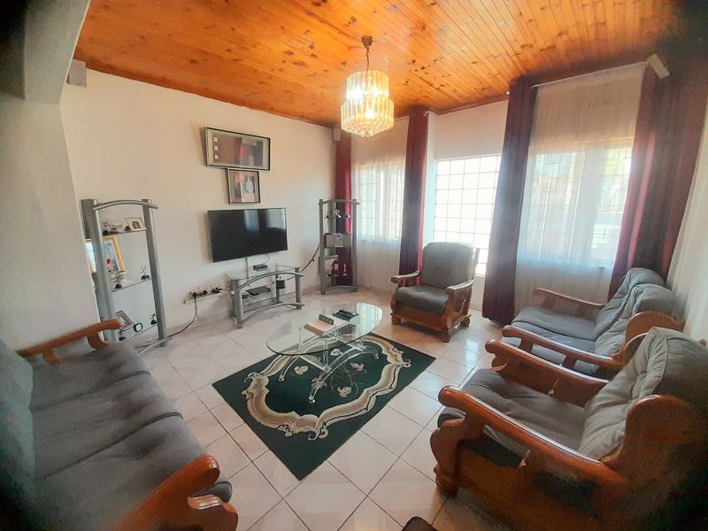 A living room featuring a warm timber tongue and groove ceiling, ceramic tiled flooring, and a decorative crystal chandelier.