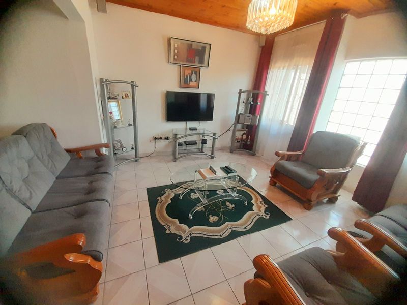 A living room featuring tiled flooring, an exposed timber ceiling, and a distinctive glass block window, providing a functional and dated living space.