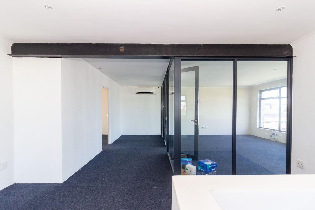 Modern office space featuring a glass partition wall, exposed steel beam, air conditioning, and neutral carpet flooring.