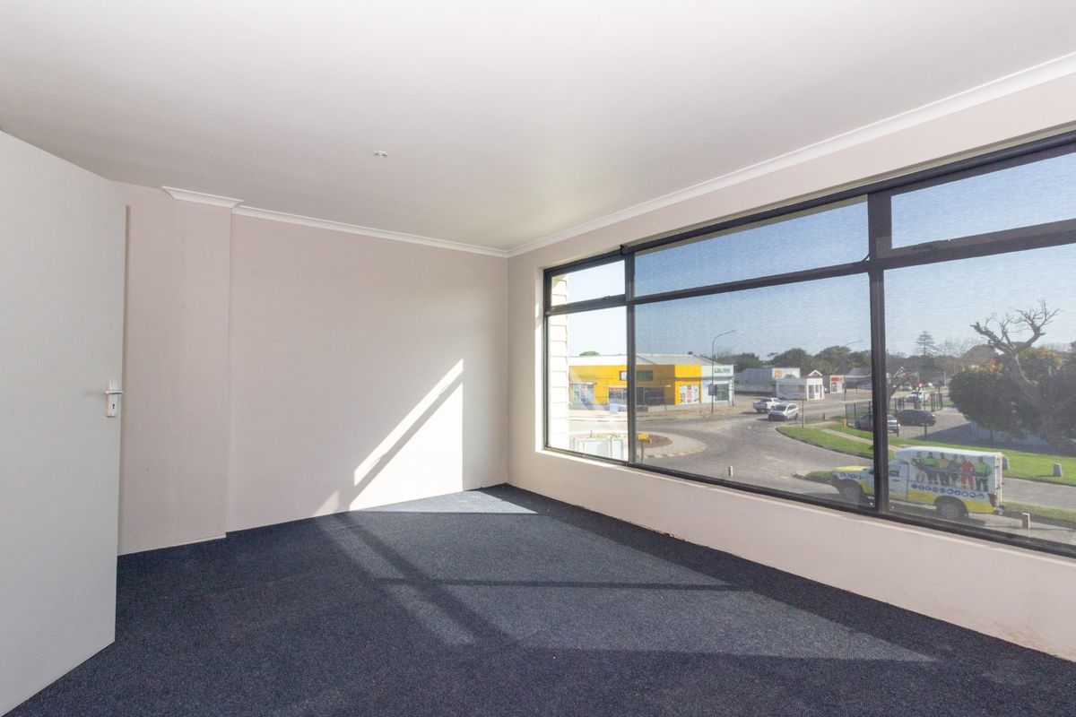A bright, empty office space featuring large windows with street views and clean carpet flooring, suitable for a professional workspace.