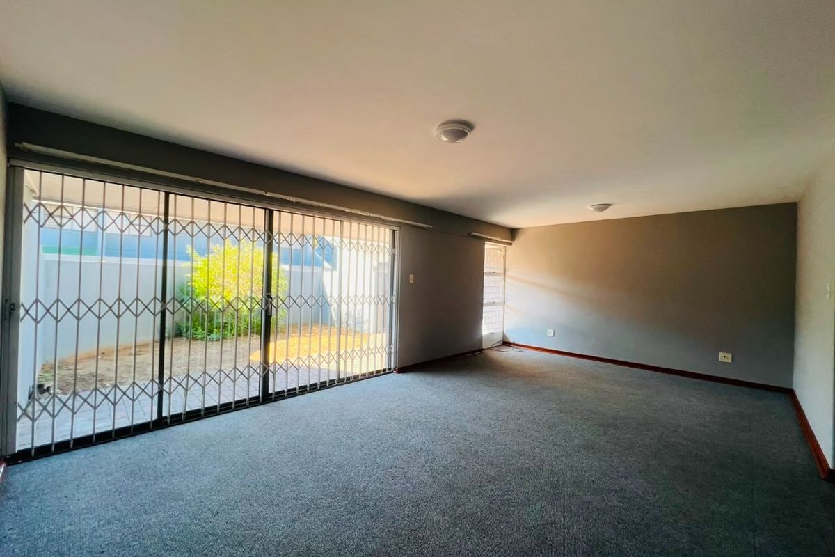 Spacious living area featuring neutral carpeting, large sliding glass doors with security gates, and direct access to a private outdoor patio space.